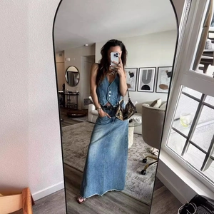 Détail d'un gilet en jean bleu foncé avec boutons blancs et jupe longue à ourlet effiloché