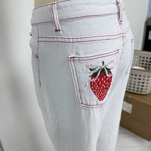 Detail of strawberry and bow embroidery with red stitching on white denim jeans pockets