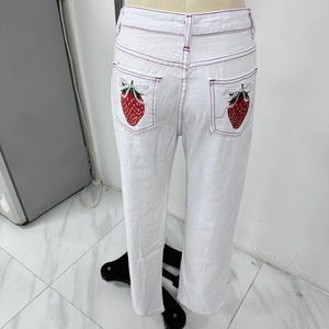 Close-up of strawberry embroidery and red contrast stitching on white denim pockets