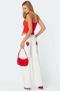 Detail showing red strawberry embroidery patch on the back pocket of white denim pants