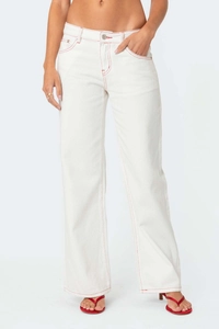 Detail of white straight-leg denim jeans with vibrant red contrast stitching and silver button