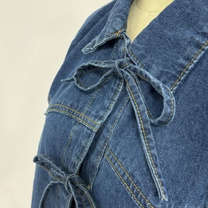 Détail d'une veste en jean avec brides à nouer et surpiqûres dorées contrastées