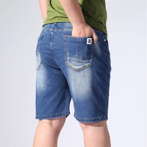 Detail of men's blue denim shorts featuring a white embroidered letter B on the back pocket