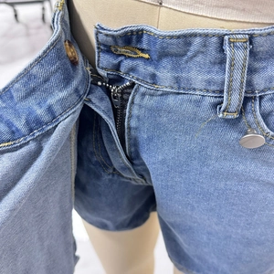 Detail of light blue denim shorts with metal zipper, brown button and silver rivets
