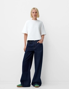 Détail du jean rétro à taille haute et jambe large porté avec un t-shirt blanc épuré