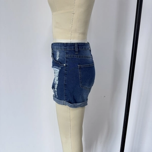 Macro detail of high waisted distressed denim shorts with frayed hems and side rip