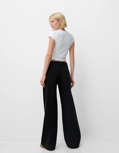 Vue arrière d'un mannequin portant un jean noir à jambes larges et un t-shirt blanc