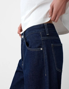 Détail de jean taille haute bleu foncé avec surpiqûres orange contrastées et rivets en métal