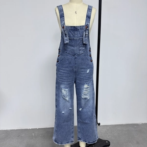 Detail of loose fit blue denim overalls with distressed rip and front patch pocket