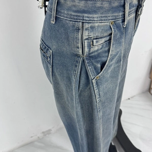 Dettaglio di jeans in denim azzurro lavato con pieghe frontali e rivetti sulle tasche