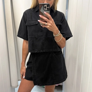 Detail of washed black denim two-piece set with V-neck shirt and high waist mini skirt