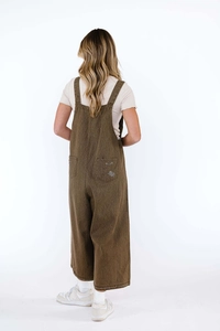 Detail of distressed back pocket on loose fit brown denim overalls with wide legs