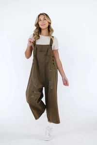 Detail of distressed retro denim overalls featuring ripped holes and a wide-leg cut