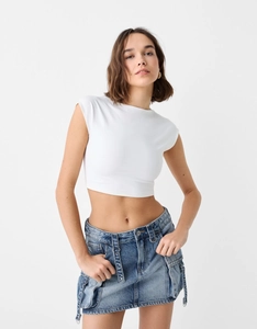 Détail du haut court blanc à manches courtes et de la jupe cargo en jean bleu à taille haute