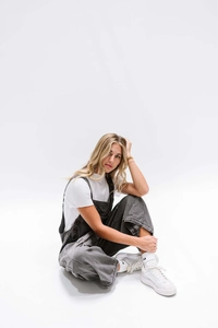 Detailed close-up of dark grey denim overalls with raw hem edges and side button accents