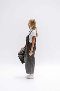Side view of distressed grey denim overalls with ripped details and metal buttons