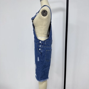 Detail of distressed blue denim overalls with ripped holes and raw hem on a mannequin