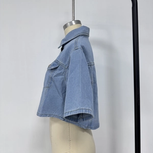 Detailed close-up of light blue washed denim crop jacket fabric and metal button closure