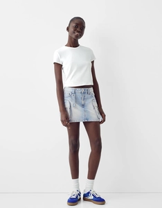 Détail d'une mini-jupe cargo en jean bleu clair avec poches latérales et texture denim