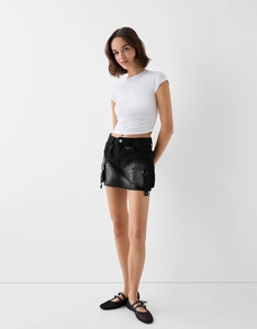 Détail d'une mini-jupe cargo en jean noir avec poches utilitaires et anneaux en métal