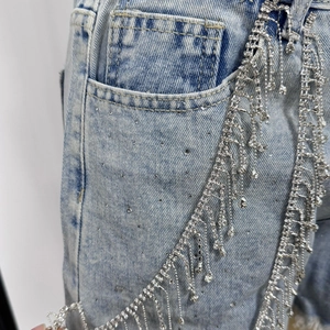 Detail of light blue denim shorts featuring sparkling silver rhinestone fringe on the pocket