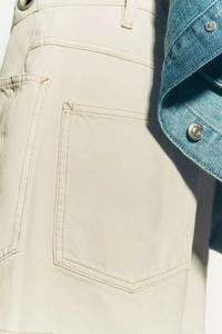 Detail view of reinforced stitching and back pocket on light beige denim shorts for women