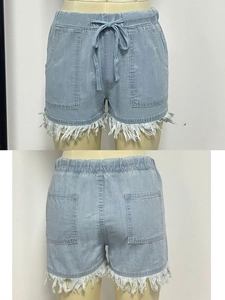Detail view of high waisted light blue denim shorts with drawstring and tassel fringe hem