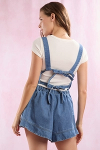 Detail of blue denim overalls back featuring double bow tie straps and elastic waist