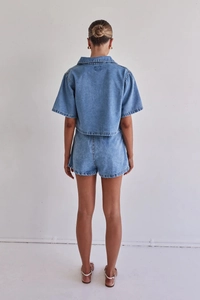 Vista trasera del conjunto vaquero azul con camisa corta y pantalones cortos de talle alto