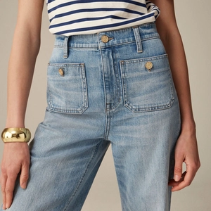Detail view of high waist light blue denim jeans with large front pockets and gold buttons