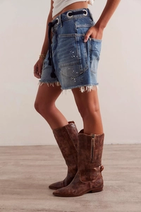 Detail of washed denim shorts with white splatter effect and brown leather boots
