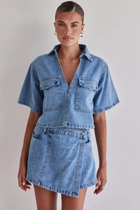 Detalle de conjunto denim azul claro con falda cruzada y camisa de manga corta