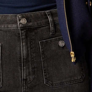 Macro detail of high-waist washed denim jeans with silver crown embossed metal button