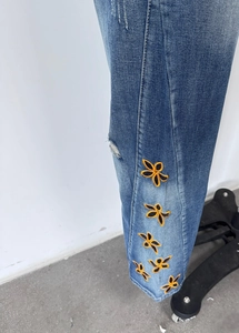 Détail d'un jean bleu à taille haute avec broderie florale orange et finitions délavées
