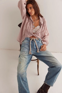 Détail montrant la texture du denim délavé avec taches de peinture et ceinture en corde