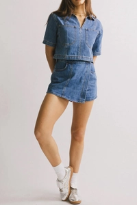 Detalle de top denim con cuello en V y falda cruzada con costuras de contraste y bolsillos