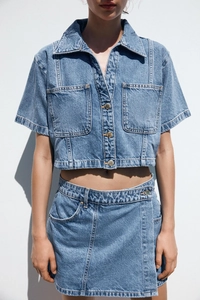 Detail of blue denim shirt with gold buttons and high-waisted skirt set on model
