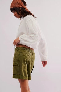 Détail d'un short cargo vert olive avec poche latérale et chemisier blanc à volants