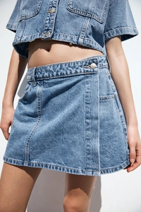 Detail of denim two-piece set featuring contrast stitching and metallic buttons