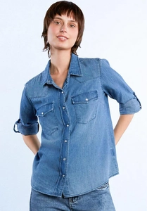 Detail of blue denim shirt featuring chest pockets with metal buttons and pointed collar