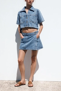 Detail of light blue denim two-piece set featuring short sleeve shirt and skirt with pockets