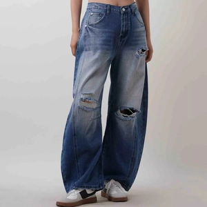 Detail of vintage washed wide-leg jeans featuring heavy distressed ripped knee textures