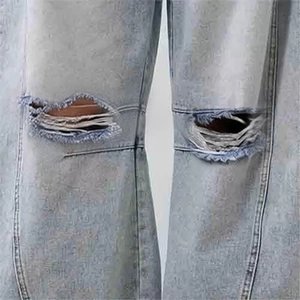 Close-up of distressed knee rip detail on light blue washed denim jeans for women
