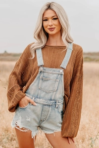 Outdoor shot of light blue washed denim overalls with distressed details and knit sweater
