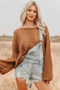 Detail of light blue distressed denim overalls with frayed edges and hollow knit sweater