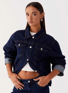 Détail d'une veste en jean bleu foncé avec coutures contrastées et poches à rabat