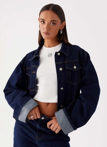 Détail de la veste en jean bleu foncé avec boutons argentés et débardeur blanc à logo