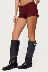 Detail view of burgundy slim fit shorts with side slits and black tall leather boots