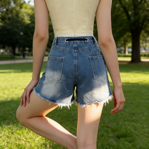 Detail view of denim shorts with frayed edges and decorative grommet eyelets on waist