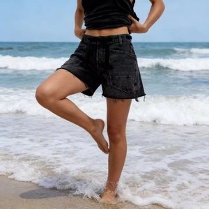 Detail of black washed denim shorts featuring frayed hems and large utility cargo pockets